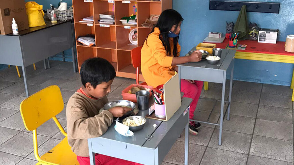 Fabian und Elisa, zwei unserer Patenkinder in Otavalo essen an ihren Pulten. Foto © Gritt Bachmann